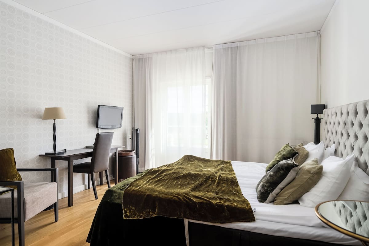 A hotel room with a bed, a desk, a chair, a television, and a window with curtains.