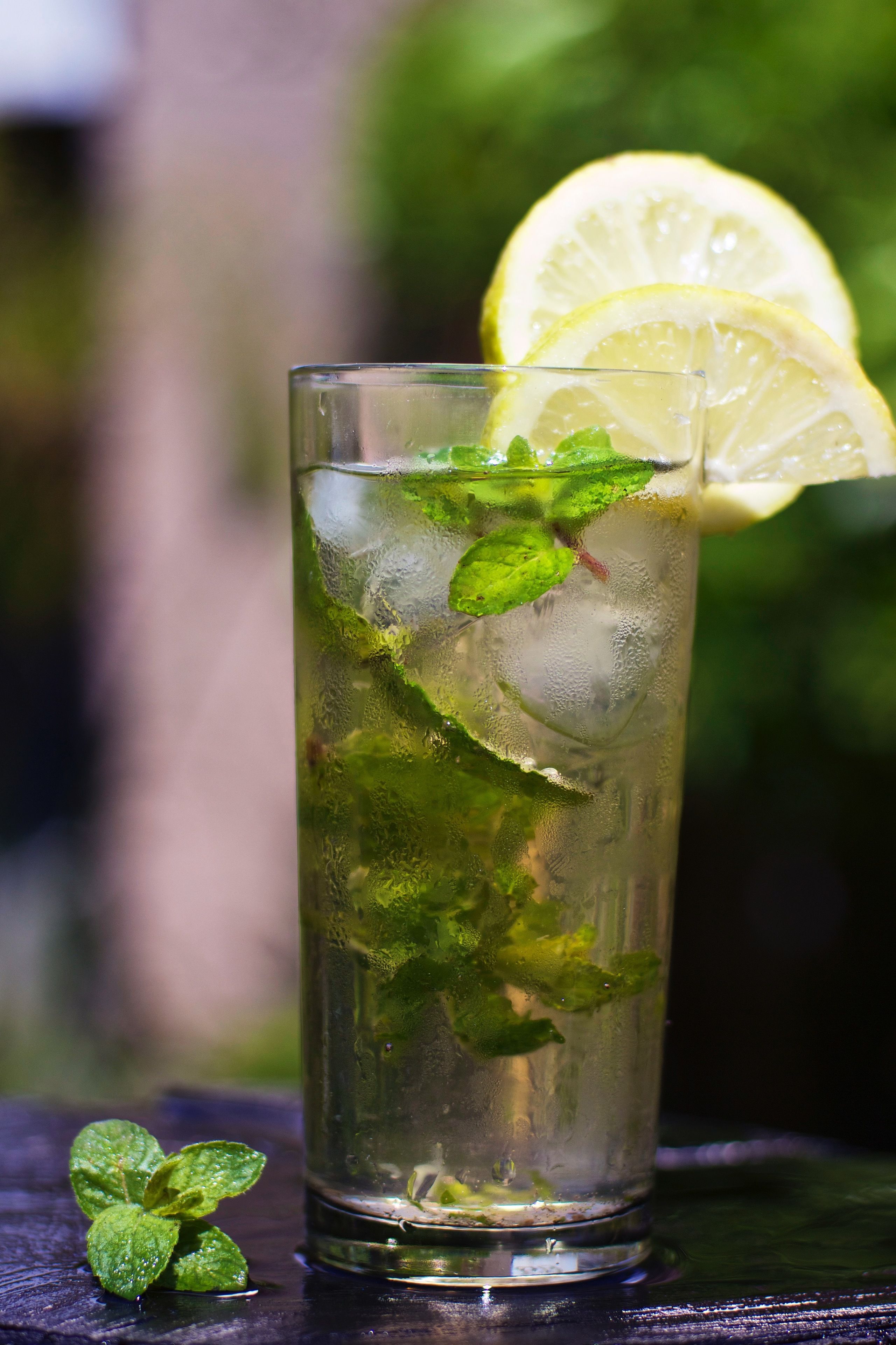 Un vaso de bebida helada con hojas de menta y una rodaja de limón, sobre una superficie de madera.