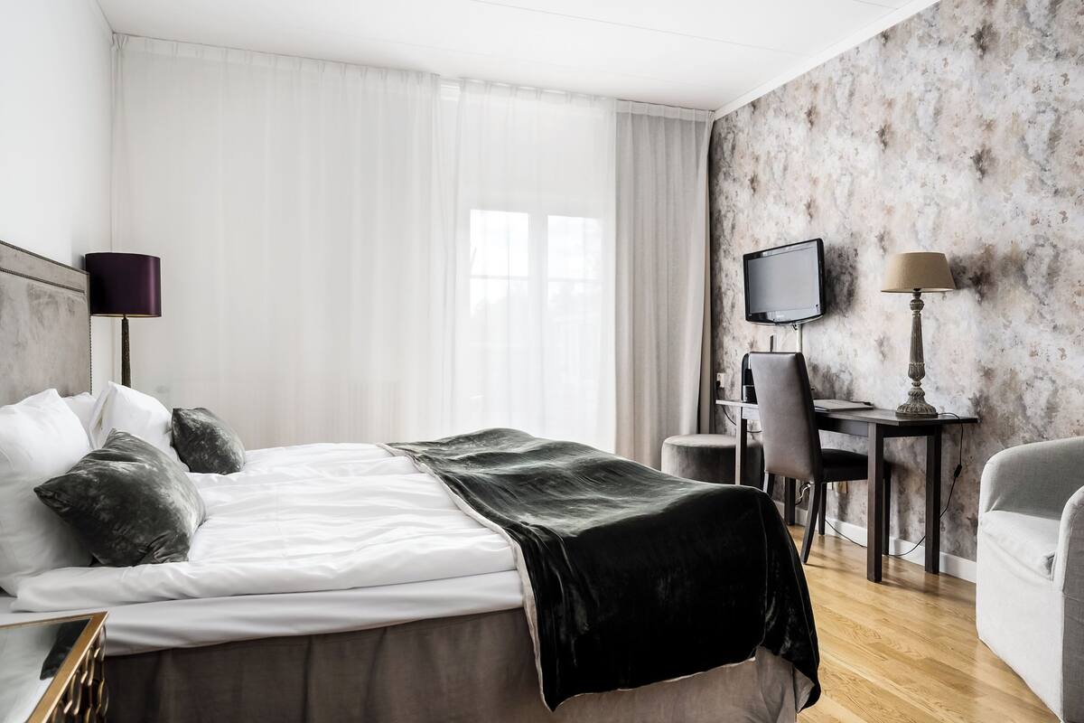 A hotel room with a bed, a desk, a chair, a TV, and a lamp.