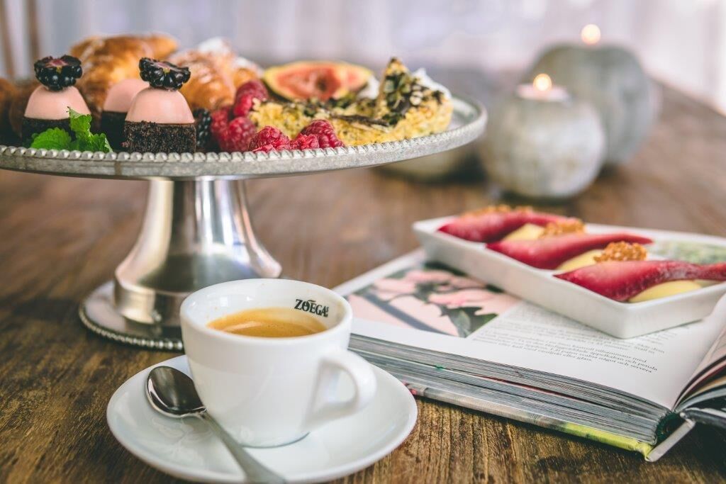A dessert plate with various pastries and fruits, a cup of coffee, and a book on a wooden table.