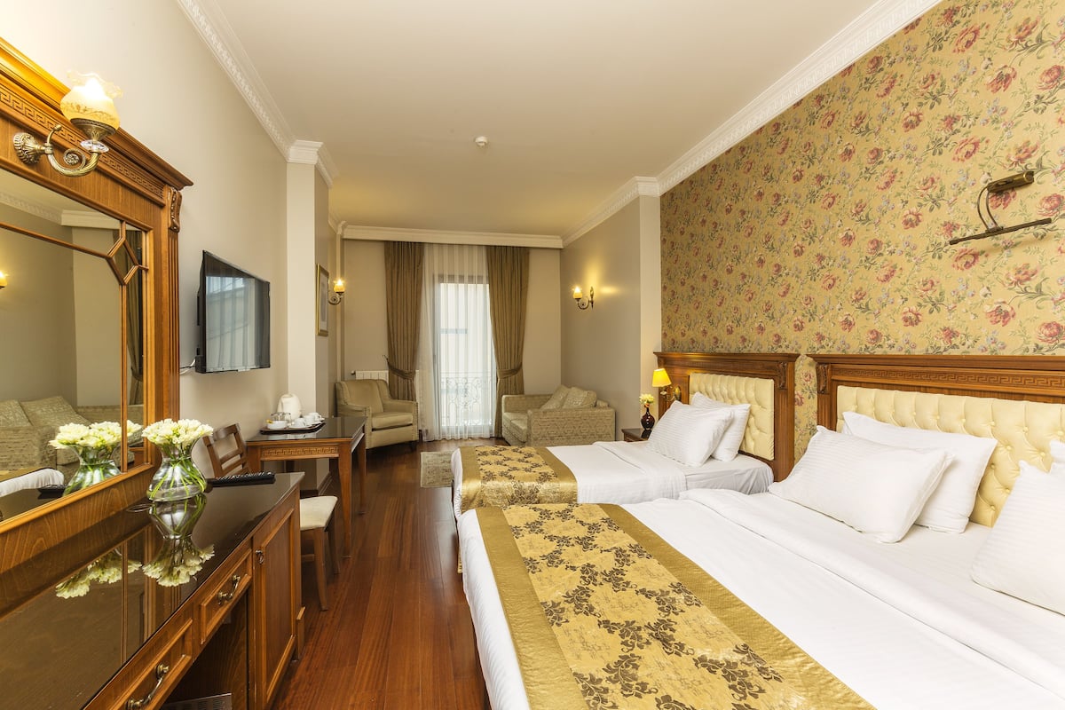 Habitación de hotel con dos camas, un escritorio, una silla, un televisor y un espejo grande.