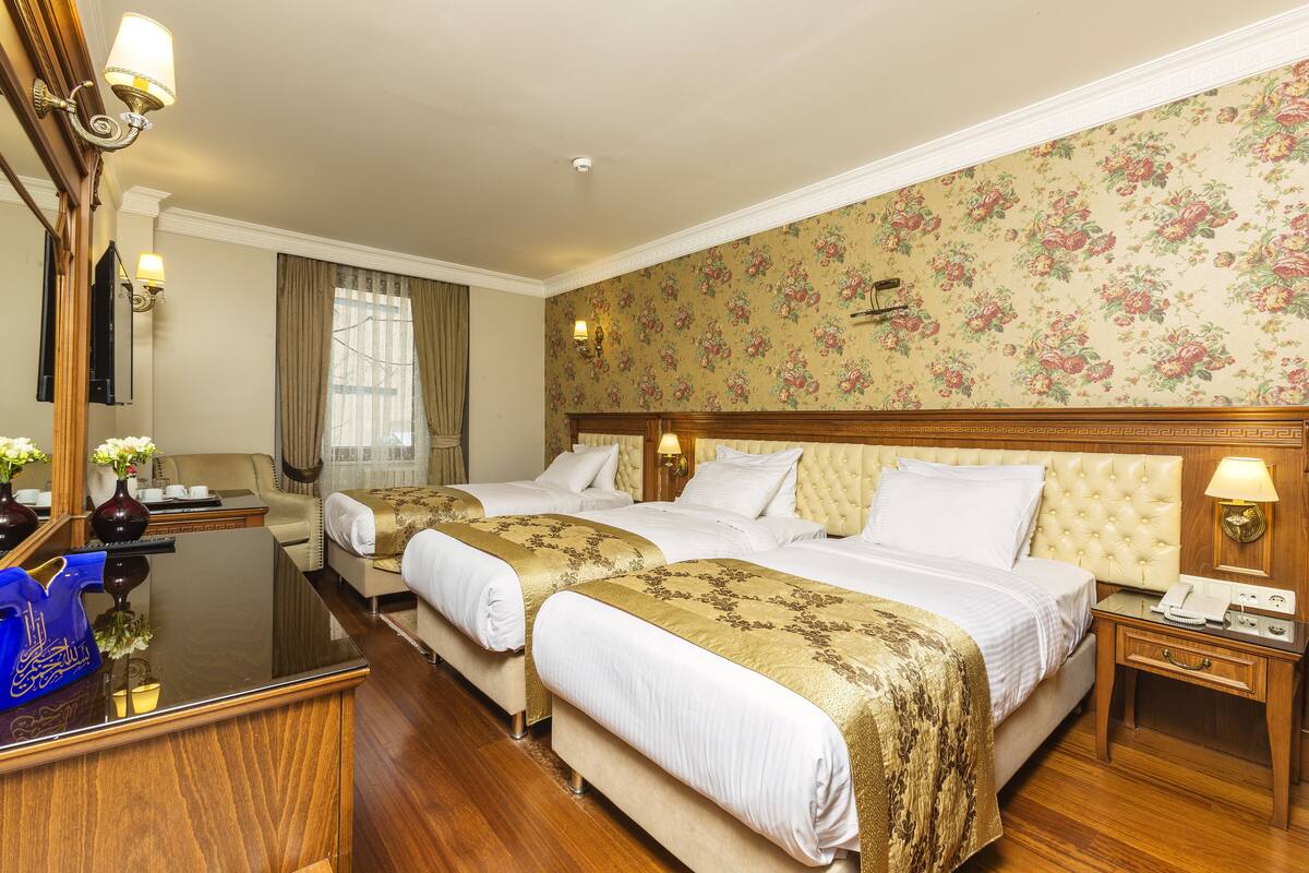 Habitación de hotel con dos camas, un escritorio de madera, un espejo y papel tapiz floral.