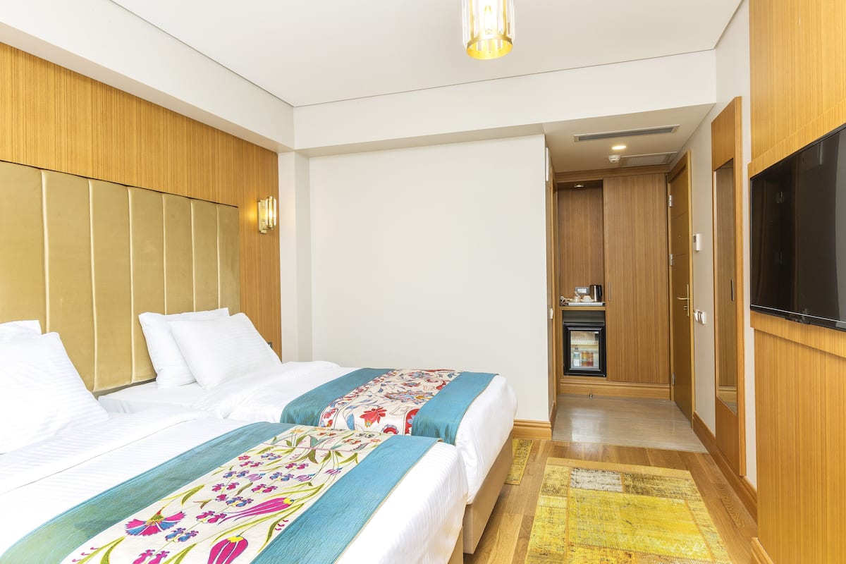 Habitación de hotel con dos camas, televisión, una pequeña kitchenette y paneles de madera.