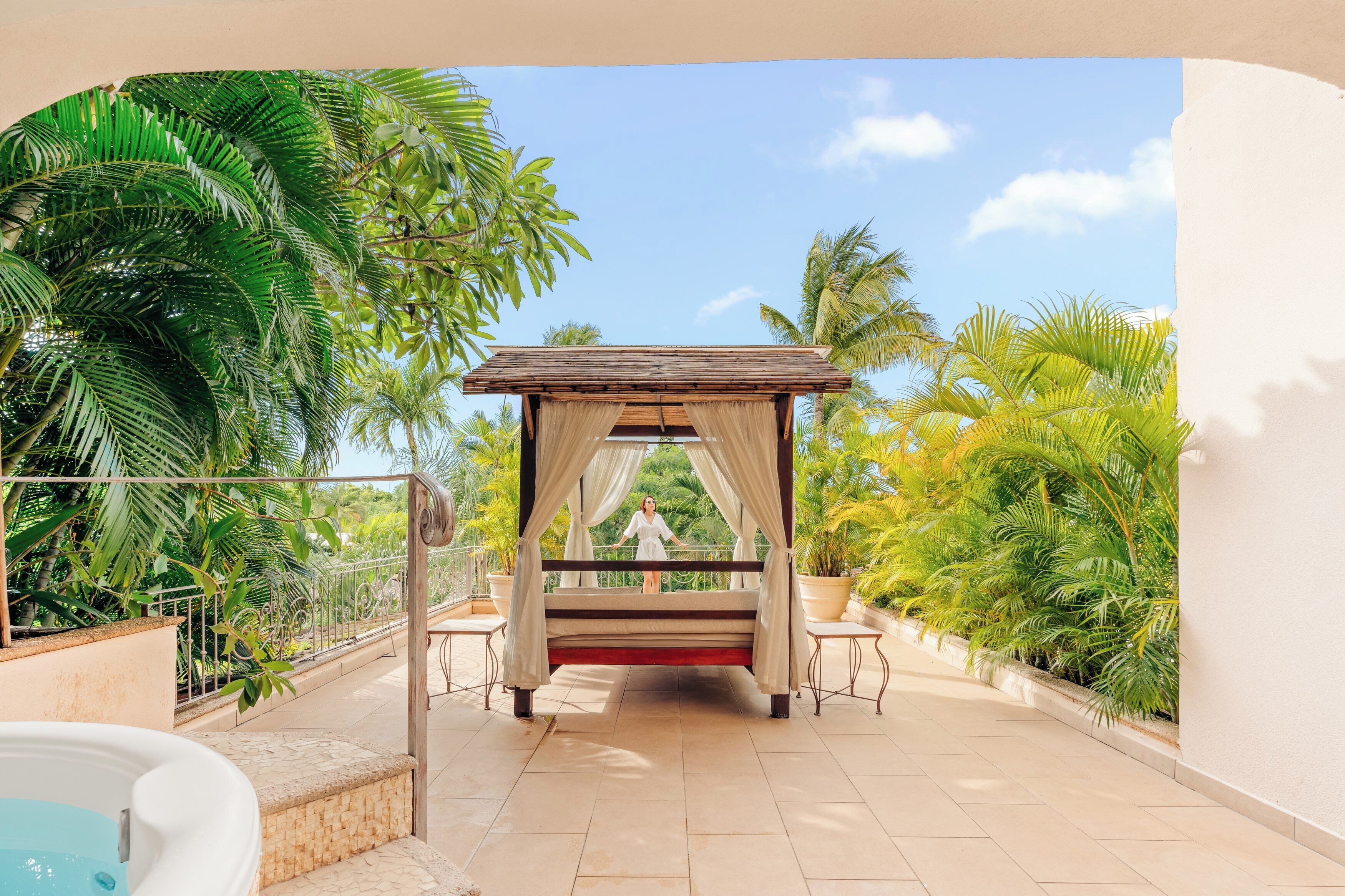 A bed under a canopy with a view of palm trees and a hot tub.