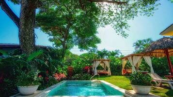 A swimming pool surrounded by lush greenery, a thatched-roof structure, and a gazebo.