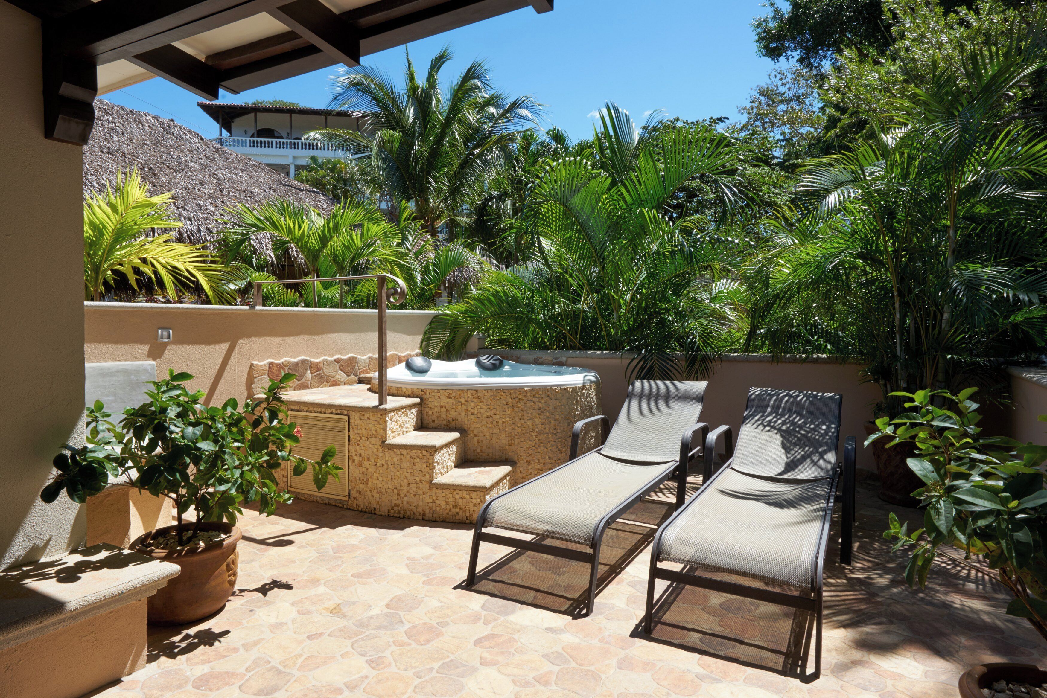 Un espace patio aménagé avec un jacuzzi, des chaises longues et des plantes en pot.