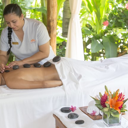 A person receiving a hot stone massage in a spa setting with a tropical backdrop.