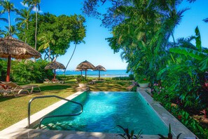 A swimming pool with a view of the ocean, surrounded by palm trees and lounge chairs. - Jardín del Edén Boutique Hotel - Adults Only (Tamarindo)