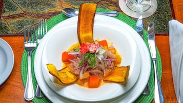 Um prato branco com um prato colorido, jogos americanos verdes e talheres de prata sobre uma mesa de madeira.