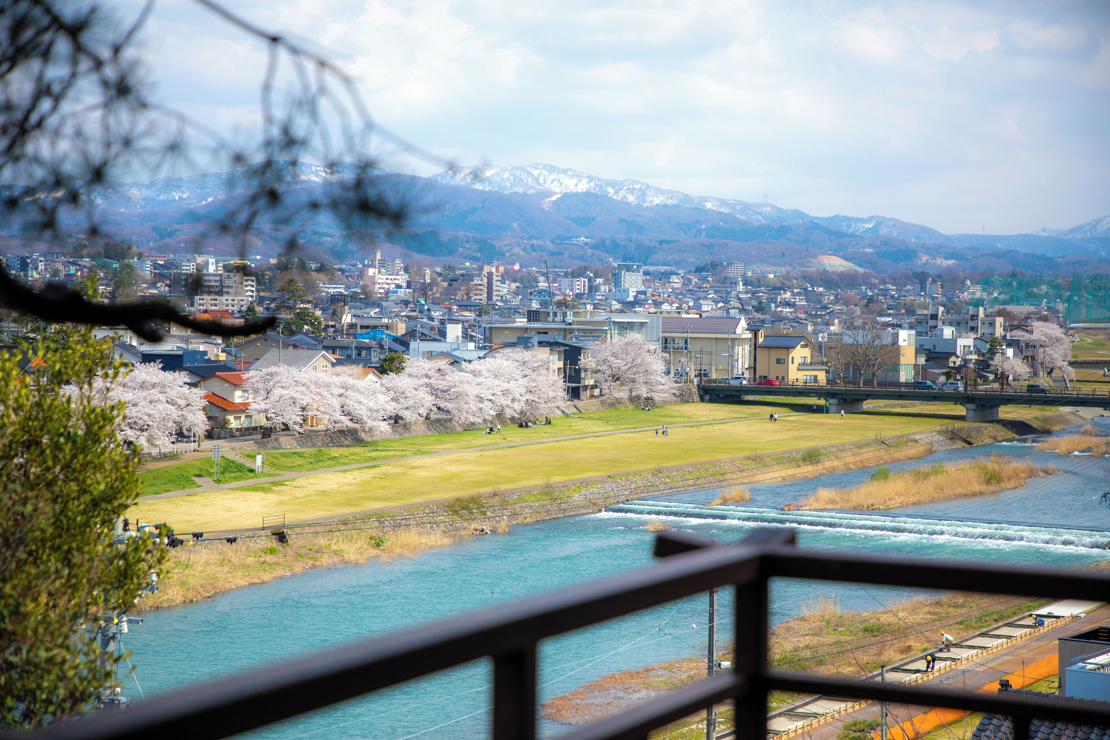 A riverside cityscape with a bridge, buildings, and snow-capped mountains in the background.