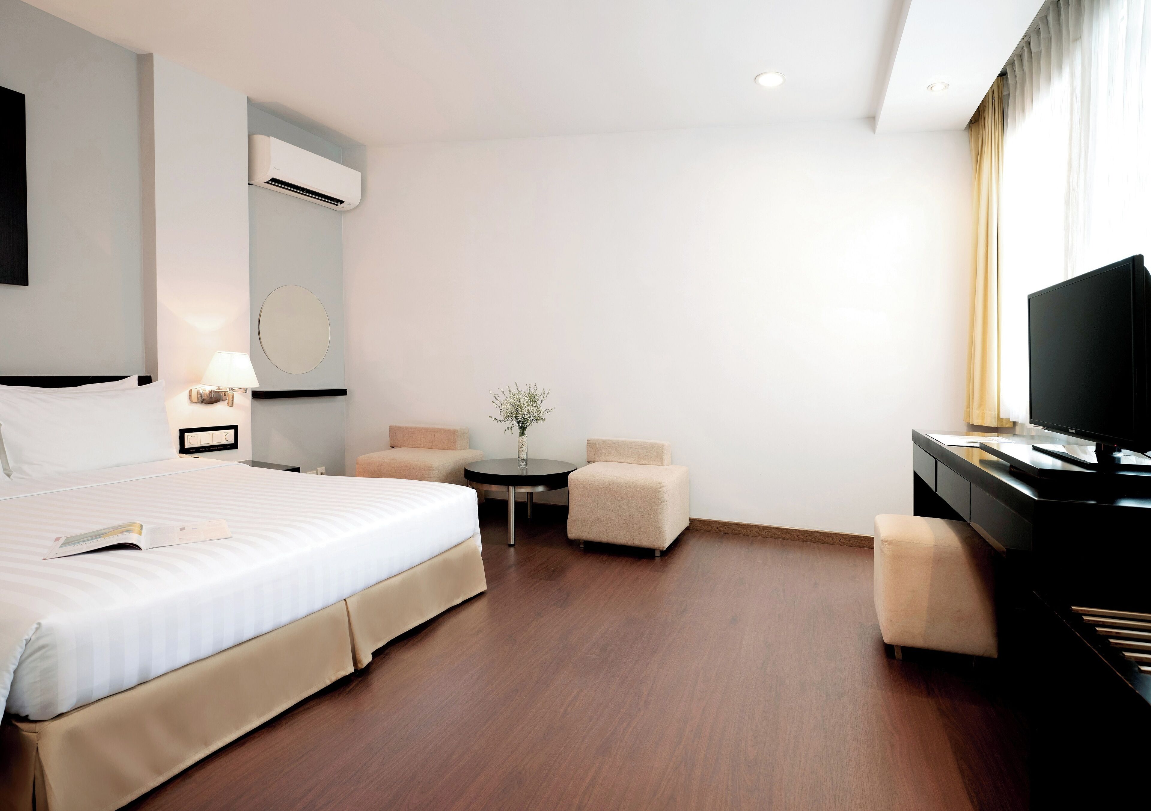 Ein Hotelzimmer mit Bett, Fernseher, Schreibtisch und einem kleinen Tisch mit einer Vase.
