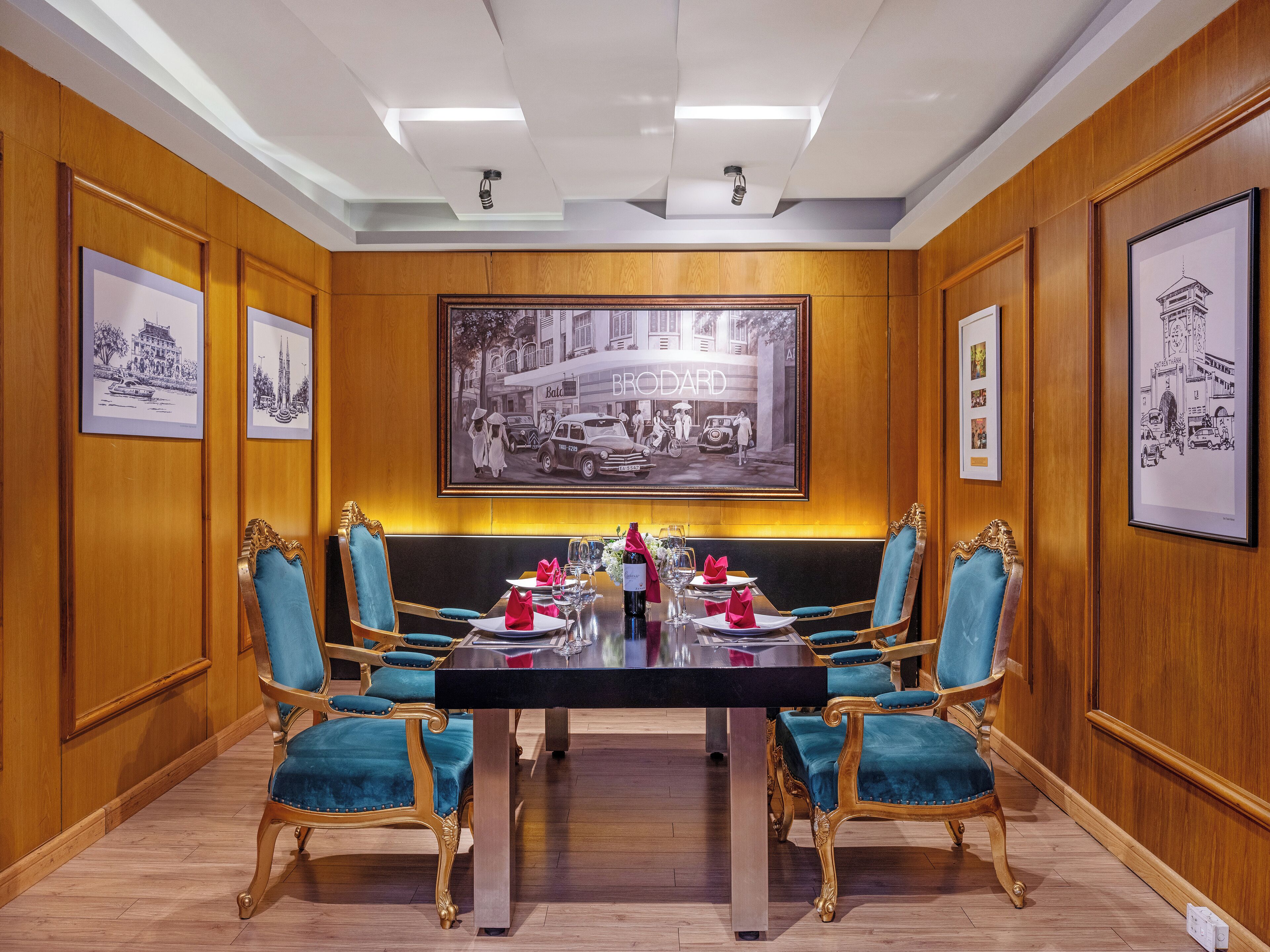 A conference room with a large table, four blue upholstered chairs, and framed pictures on the walls.