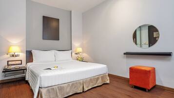 A hotel room with a bed, bedside lamps, a nightstand, a mirror, and a small orange ottoman.