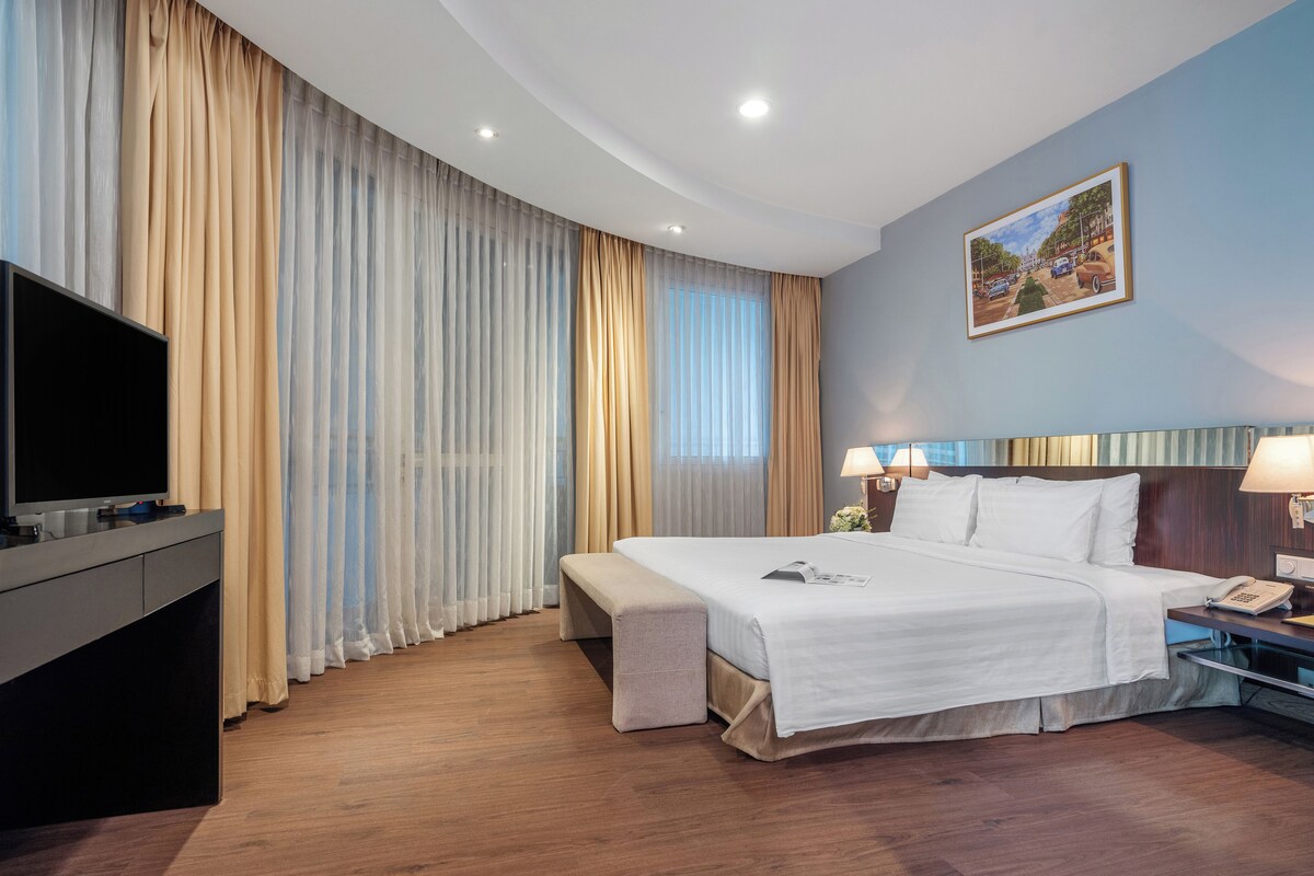 Quarto de hotel com cama, abajures, televisão e um quadro na parede.