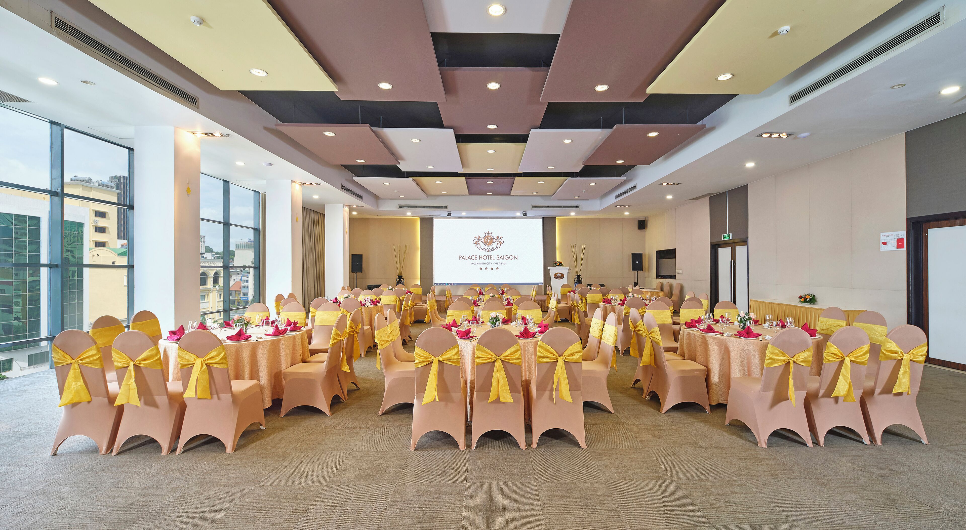 Une salle de conférence à l’hôtel Palace Saigon, avec des tables disposées pour une réunion, de grandes fenêtres et un écran de présentation.