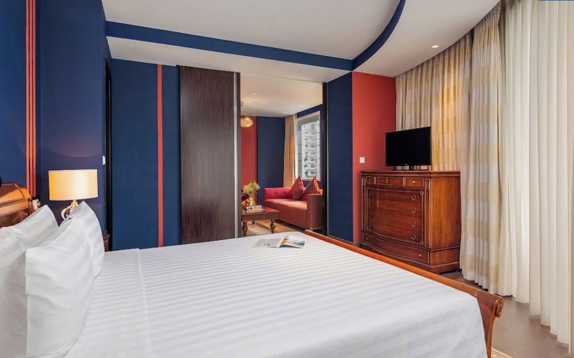 A hotel room with a large bed, a television, a wooden dresser, and a view of the city through the window.