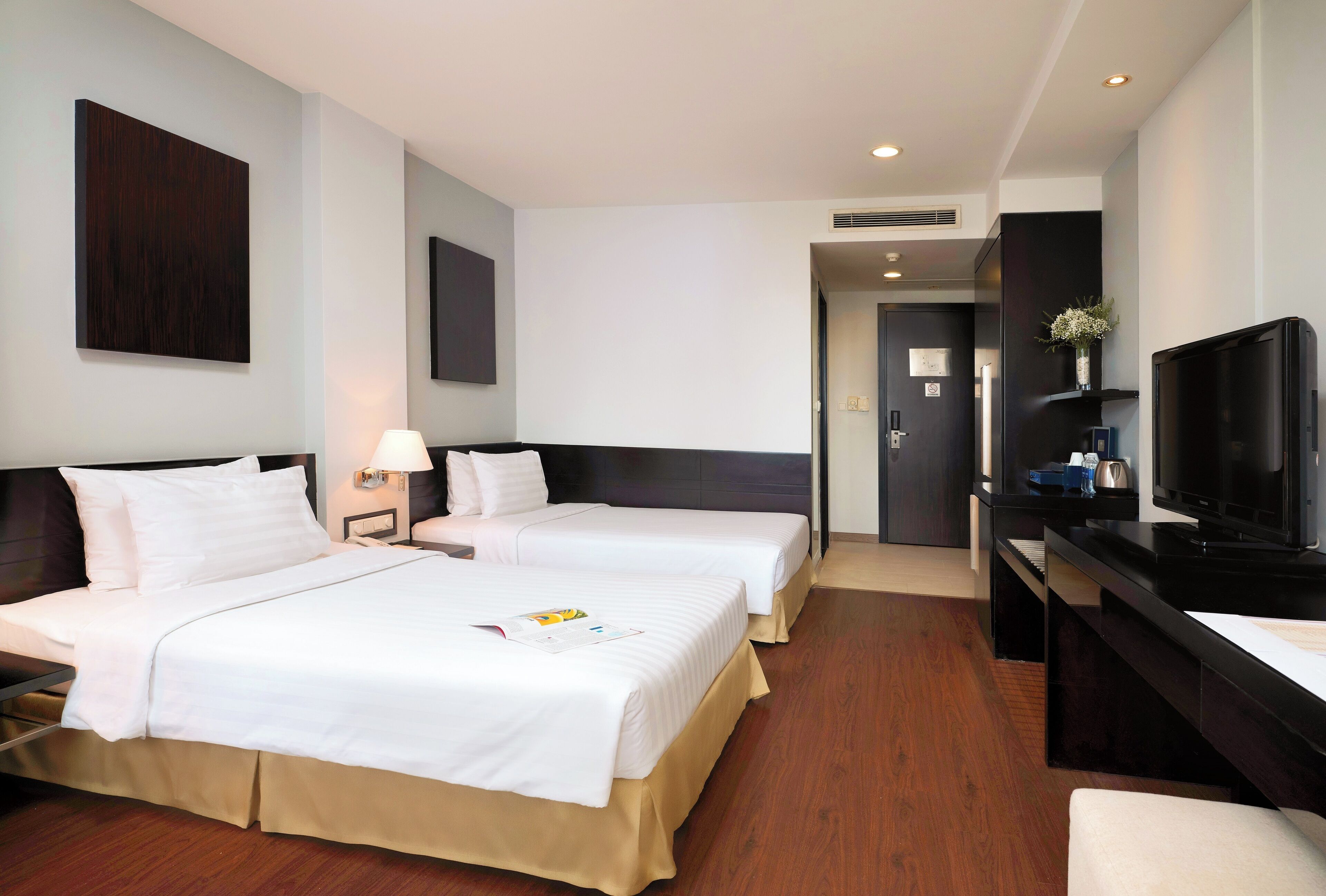 A hotel room with two beds, a desk, a television, and a door leading to a bathroom.