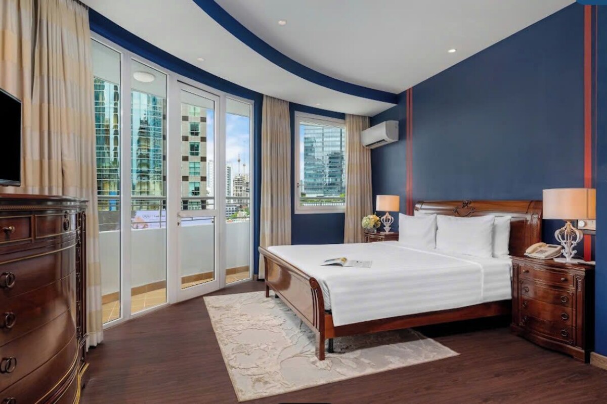 Quarto de hotel com uma cama grande, cômoda, mesa de cabeceira e televisão.