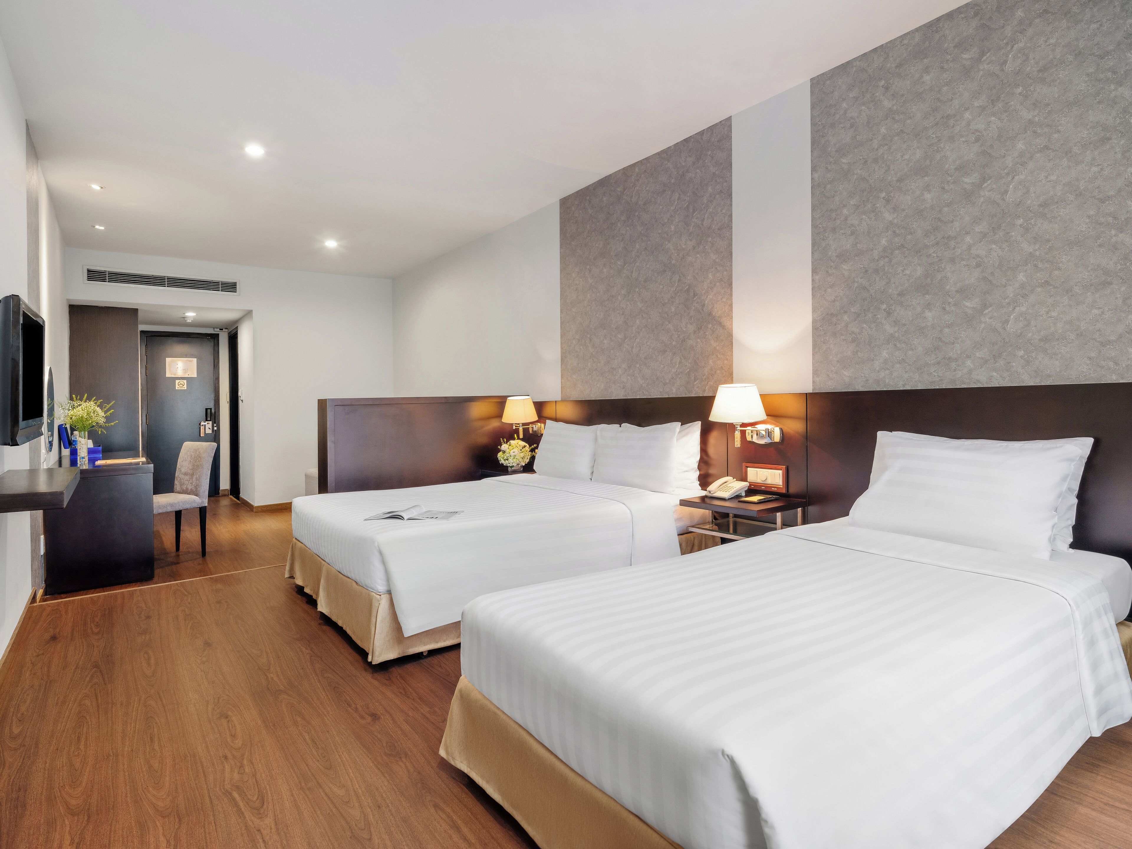 Habitación de hotel con dos camas, un escritorio, una silla y un televisor.