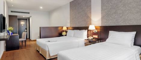 Habitación de hotel con dos camas, un escritorio, una silla y un televisor.