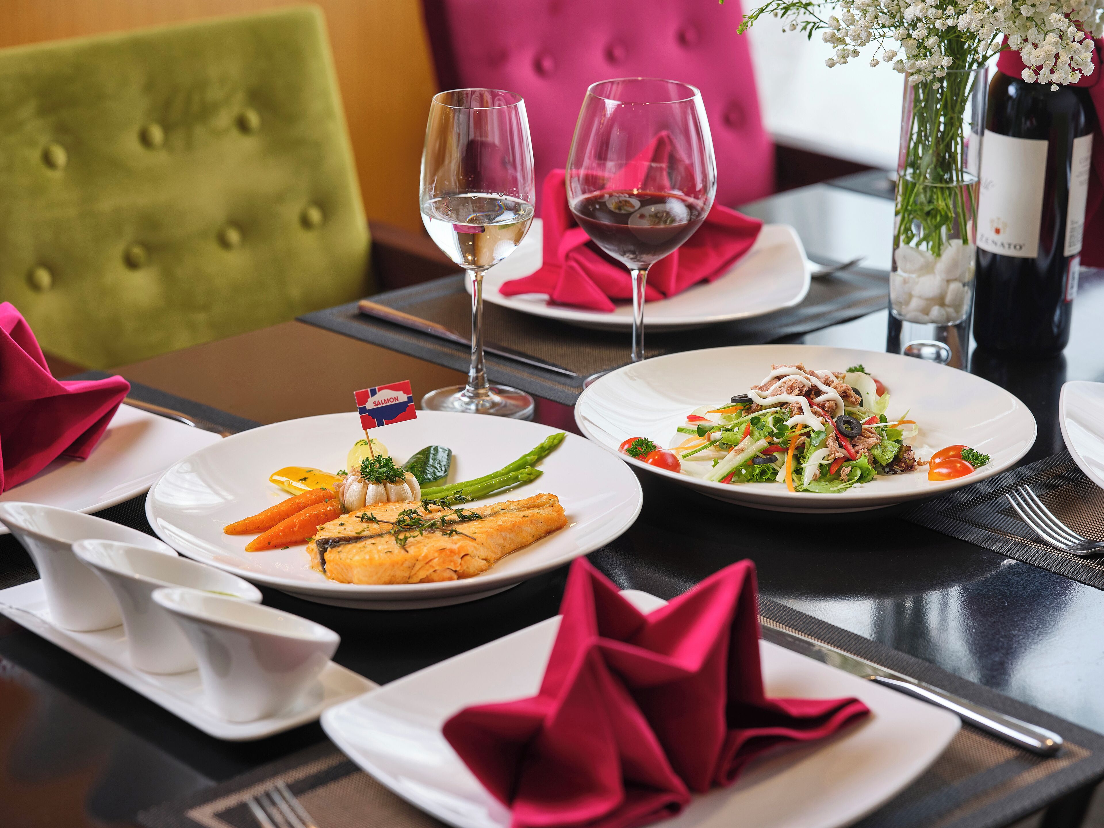 A dining table with plates of food, glasses of wine, and a bottle of wine.