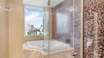 Un baño moderno con un jacuzzi de vidrio, zona de ducha con azulejos y vistas a la ciudad a través de un ventanal grande.