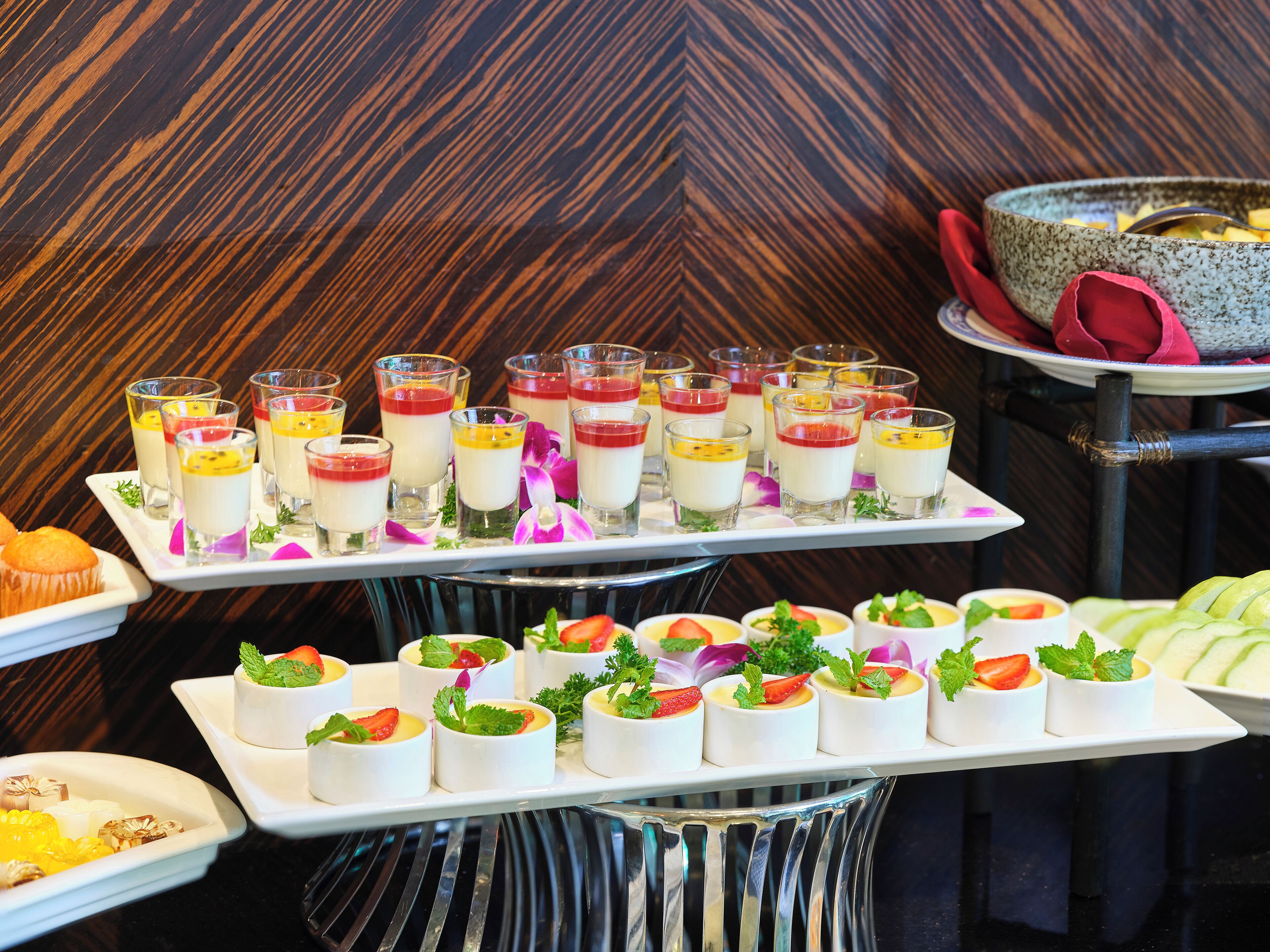 Un buffet proposant une variété de desserts et de hors-d'œuvre, notamment de petites coupes de crème anglaise et des desserts garnis de fruits, présentés sur un plateau.