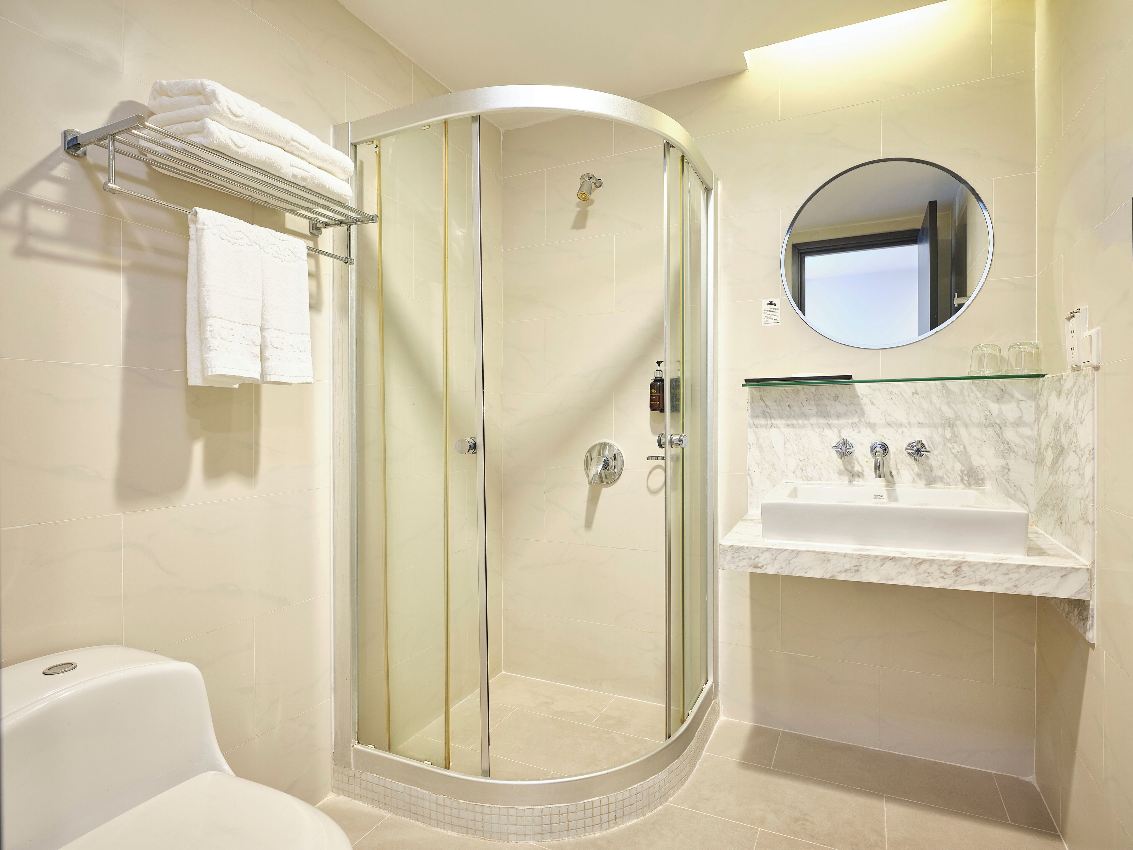 A modern bathroom with a glass-enclosed shower, a white sink, and a round mirror.