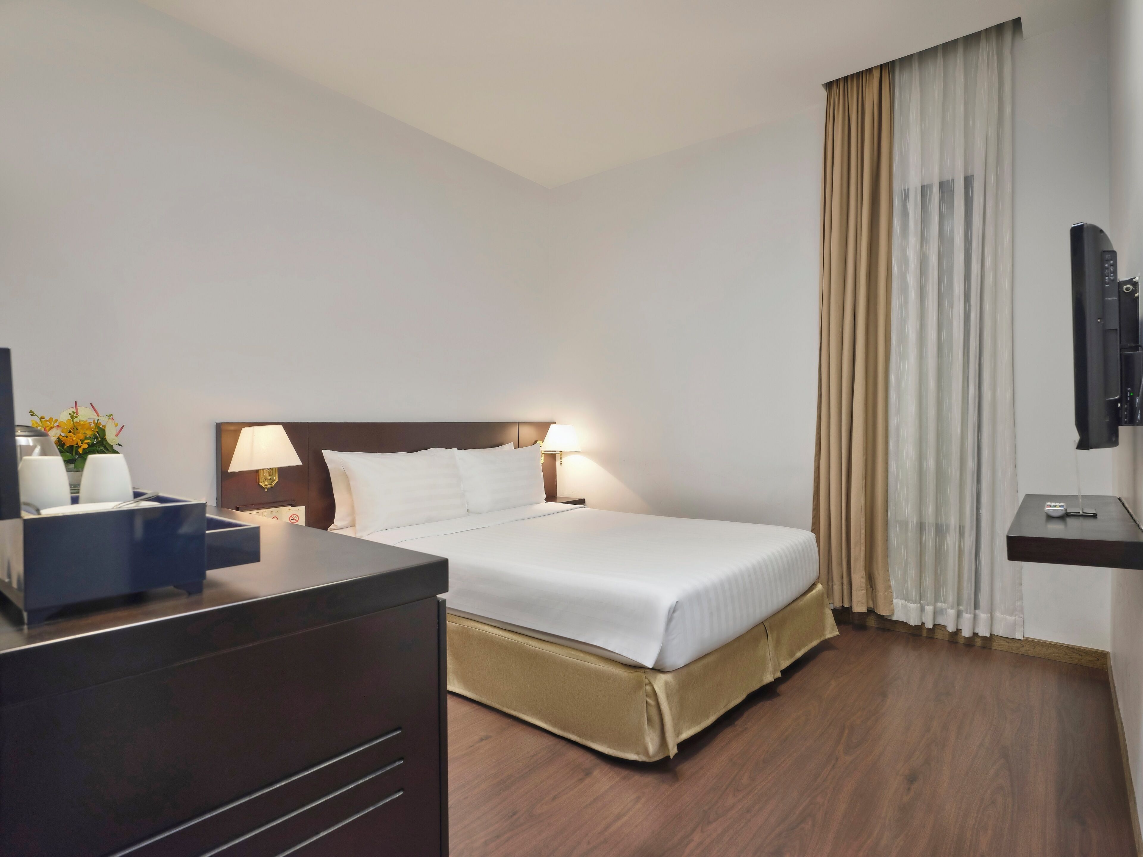 Hotelkamer met een bed, nachtlampjes, een televisie en een bureau met een bloevas.