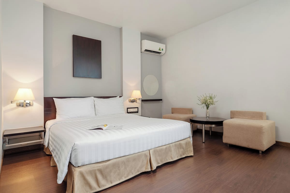 Ein Hotelzimmer mit einem großen Bett, Nachttischlampen, einem kleinen Tisch, einem Sessel und einer Klimaanlage.