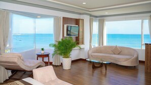 A modern living room with a large window offering a view of the sea, a comfortable sofa, a chair, and a small table with a plant. - Saigon Ninh Chu Hotel & Resort (Ninh Chu)
