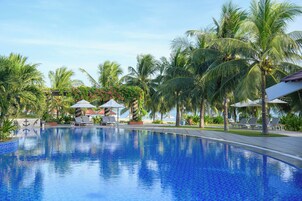 A swimming pool with lounge chairs and umbrellas, surrounded by palm trees and a clear sky.