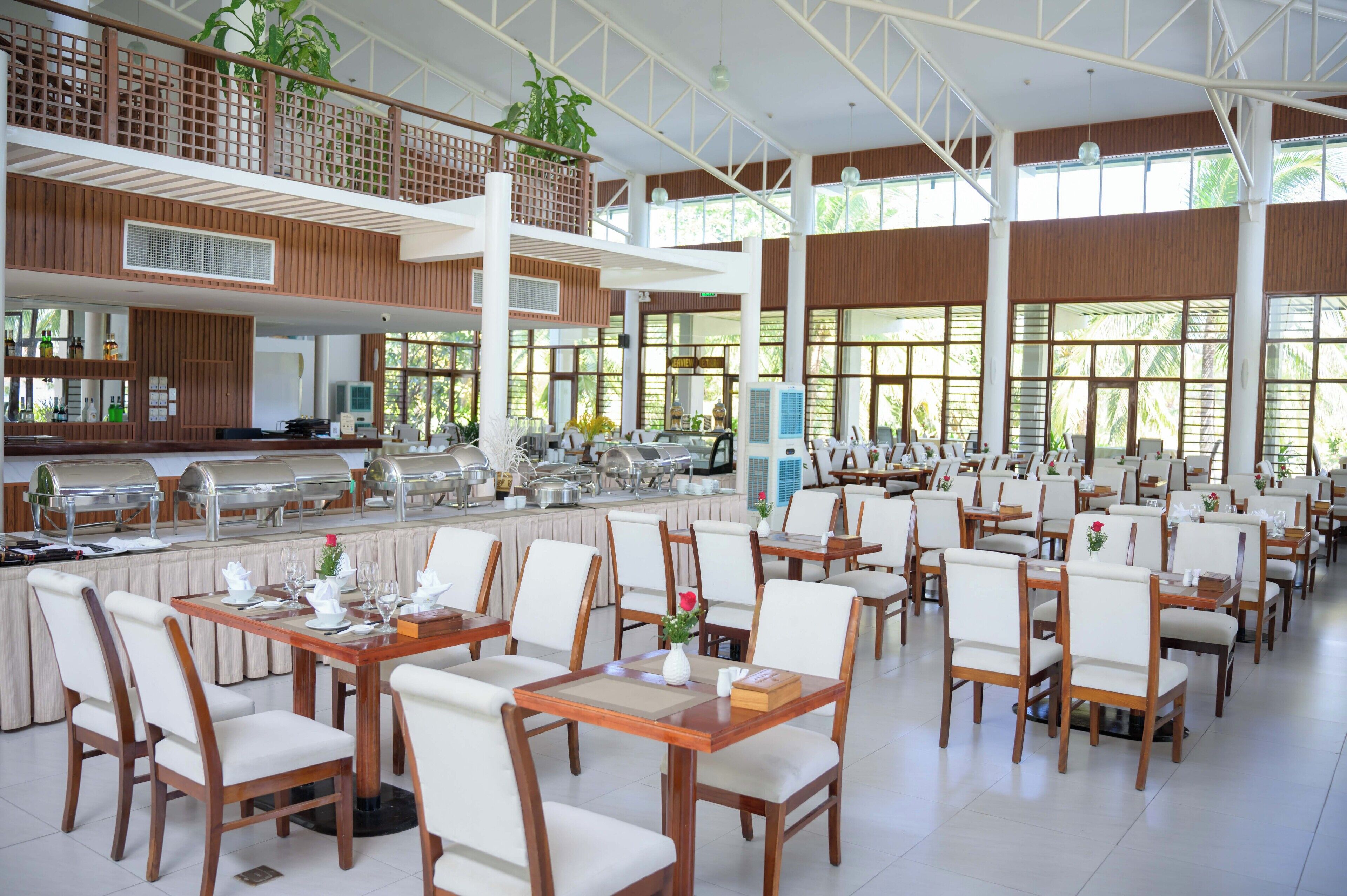 A spacious dining area with multiple tables and chairs, a buffet setup, and large windows allowing natural light.