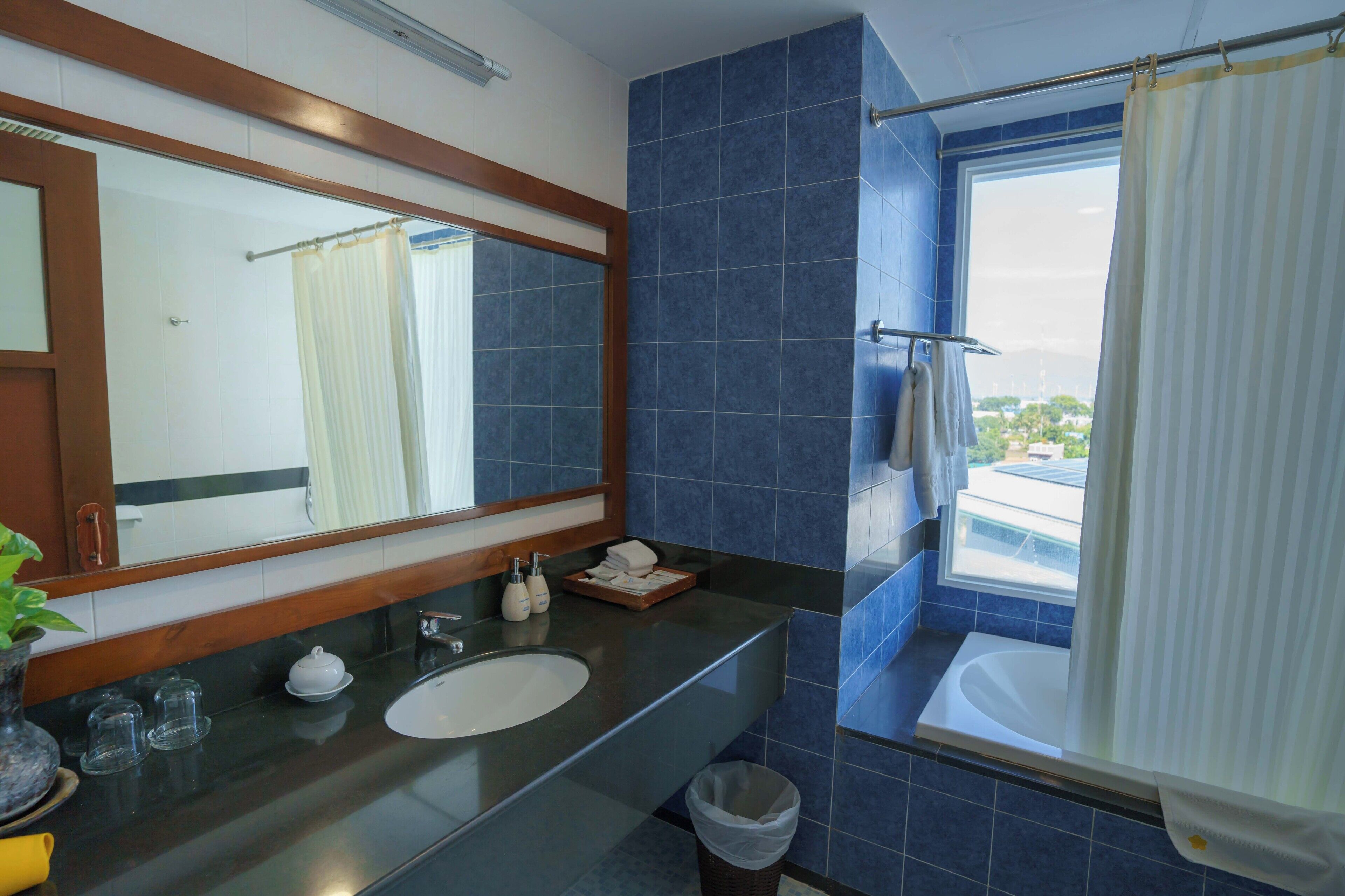 A bathroom with a large mirror, a sink, a bathtub, and a window with a view of buildings.