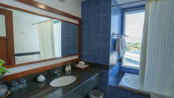 A bathroom with a large mirror, a sink, a bathtub, and a window with a view of buildings.