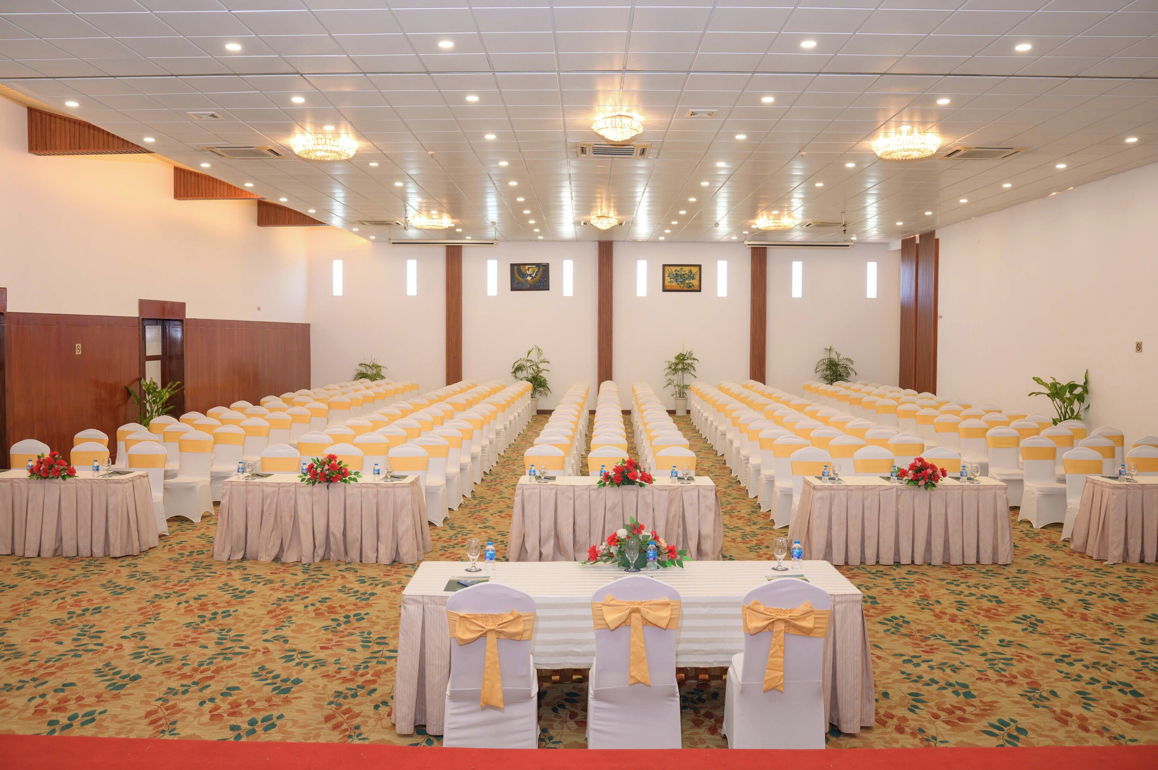 A conference room with rows of tables, each with a white tablecloth and yellow sashes.