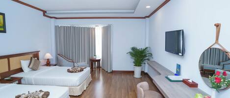 A hotel room with two beds, a TV, a mirror, a plant, and a fruit bowl.