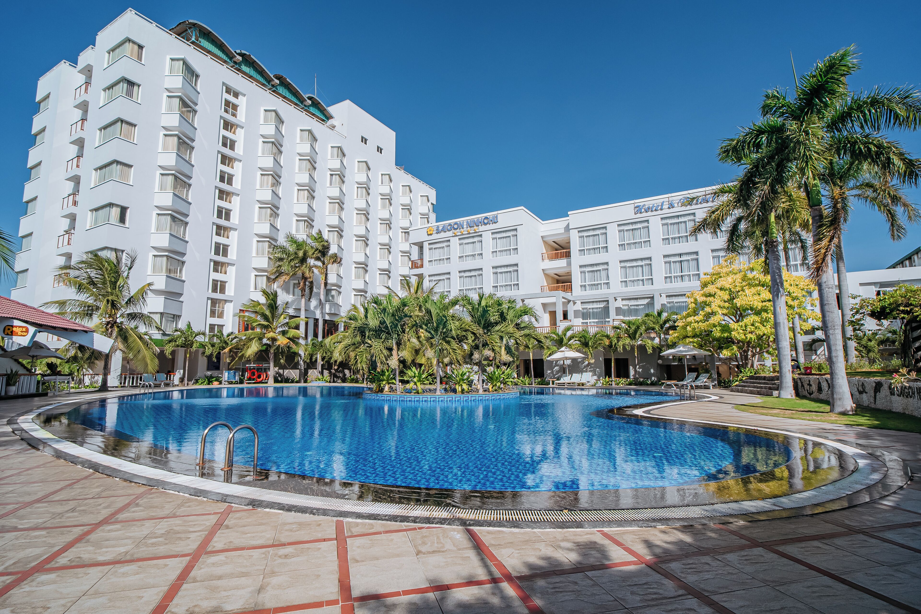 Un hotel con piscina rodeado de palmeras y un edificio grande con balcones.