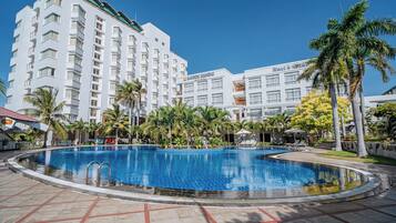 Un hotel con piscina rodeado de palmeras y un edificio grande con balcones.