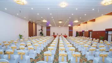 A large hall with rows of white chairs with yellow sashes, a carpeted floor, and chandeliers on the ceiling.