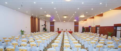 Un amplio salón con filas de sillas blancas con lazadas amarillas, suelo alfombrado y candelabros en el techo.
