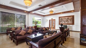 A spacious living area with multiple sofas and armchairs, a coffee table, and a large window with blinds. - Kingdom Angkor Hotel (Siem Reap)