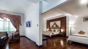 A hotel room with a large bed, a smaller bed, a sofa, a desk, and a chair. There is a window with curtains and a painting on the wall. - Kingdom Angkor Hotel (Siem Reap)