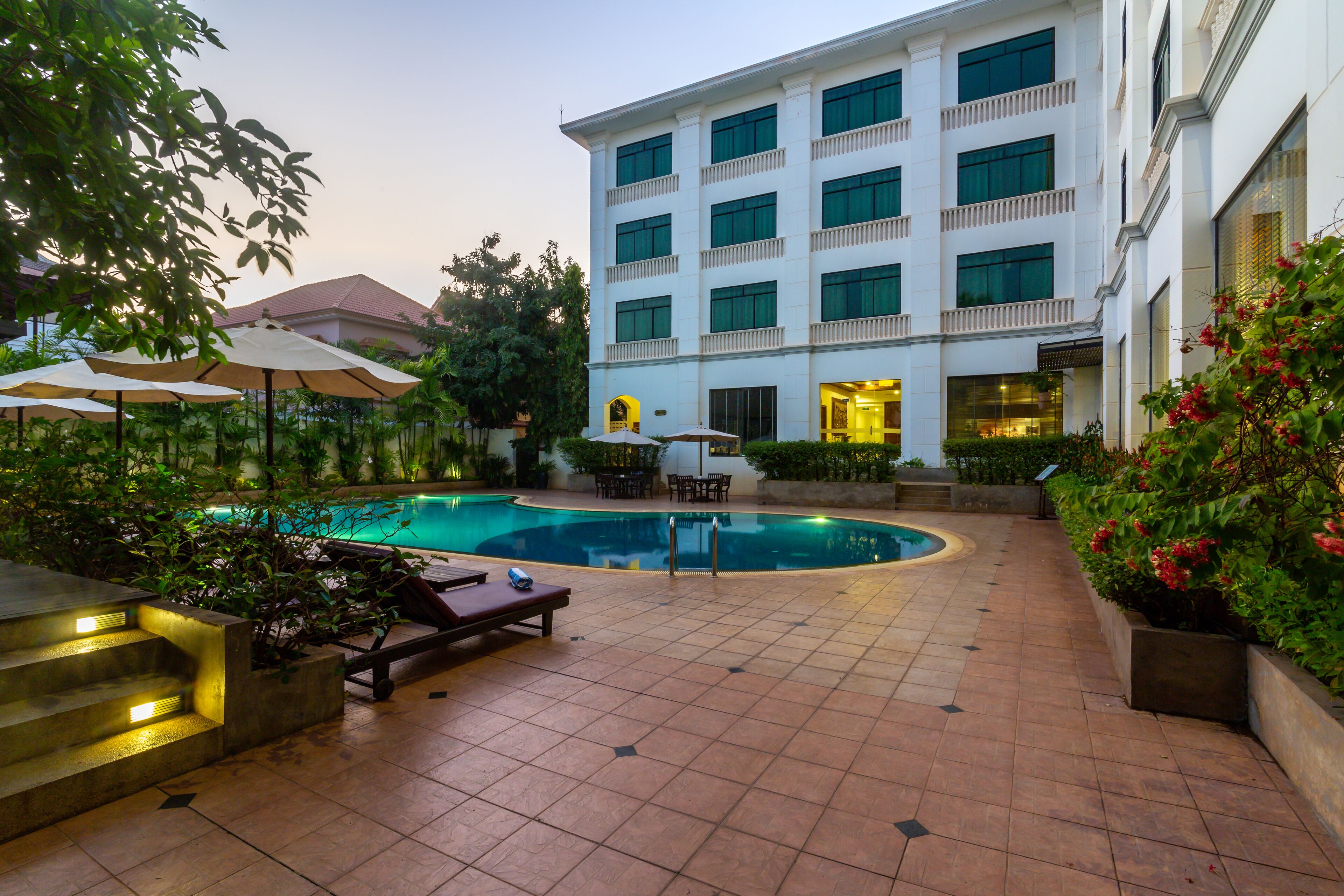 A hotel courtyard with a swimming pool, outdoor seating, and a large building with multiple balconies.