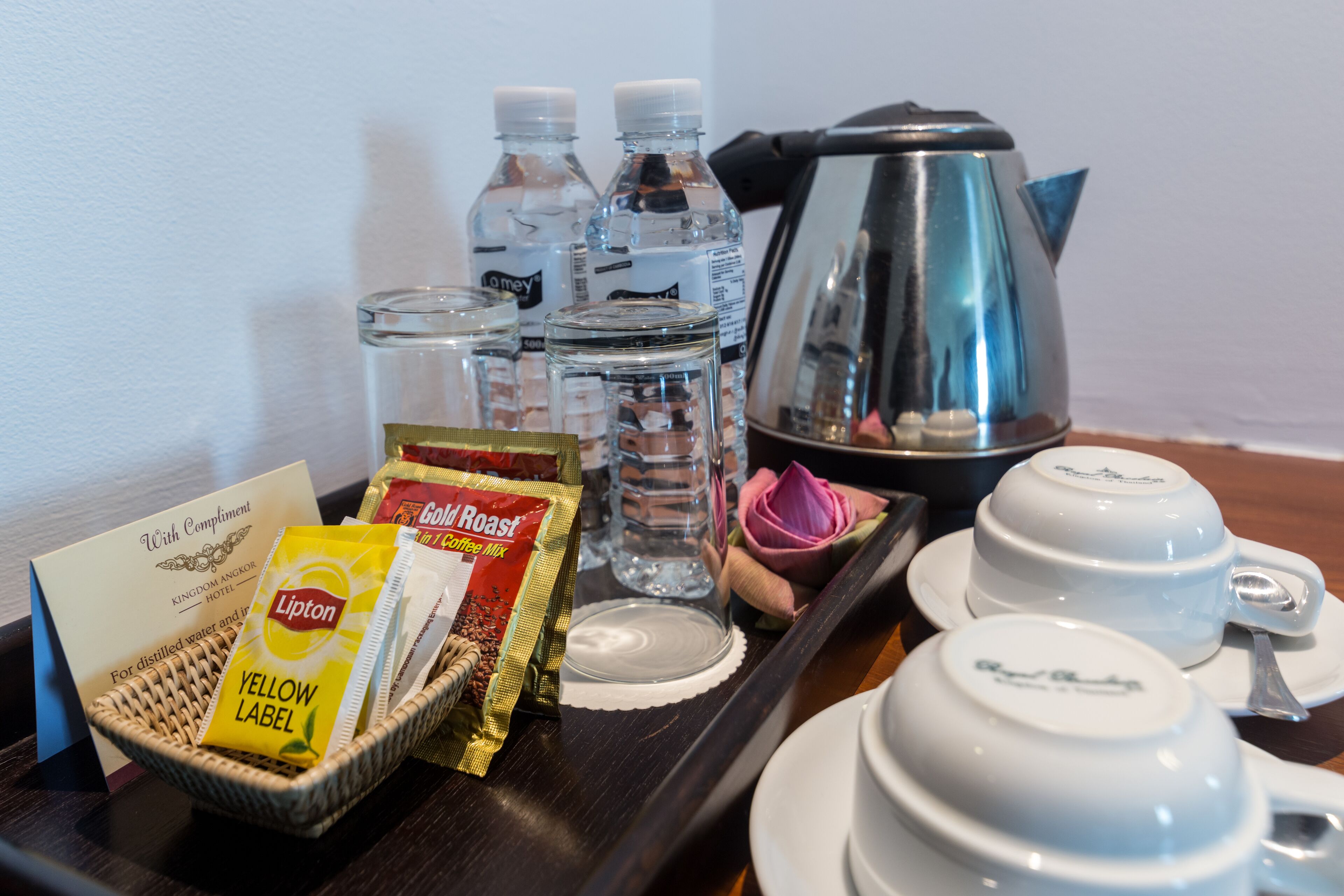 A tray with a coffee pot, teacups, water bottles, Lipton tea bags, and a rose.