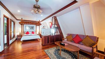 A bedroom with a bed, wooden floor, ceiling fan, and a sofa with cushions.