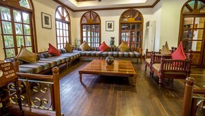 A spacious room with a large sectional sofa, a wooden coffee table, and a traditional wooden chair. - The Suite By Royal Crown Hotel (Siem Reap)
