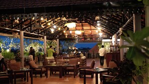An outdoor café with wooden furniture, a tiled floor, and hanging lights. - The Suite By Royal Crown Hotel (Siem Reap)
