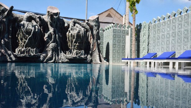 A pool with a stone wall and blue lounge chairs. - The Suite By Royal Crown Hotel (Siem Reap)