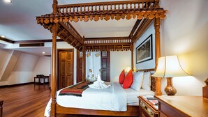 A four-poster canopy bed with a wooden finish, a nightstand with a lamp, and a framed picture on the wall. - The Suite By Royal Crown Hotel (Siem Reap)
